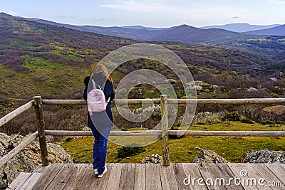 Woman with her back turned at a viewpoint contemplating the views of the green mountain landscape. La Hiruela Madrid Stock Photo