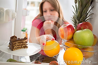 Woman hesitating whether to eat cake or orange Stock Photo