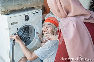 Woman in the hijab looks at the washing machine being repaired by an electronics repairman Stock Photo