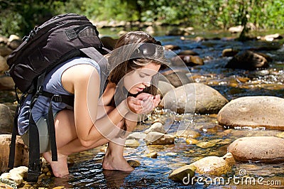Woman hiker with bag drinking water from stream in nature Stock Photo