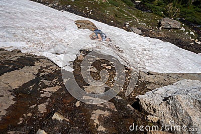 Woman hiker gets stuck on a cliff in a snowfield. Concept for dangerous hiking, hiking solo Stock Photo