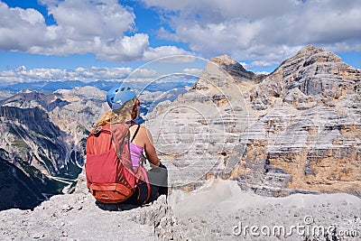 Woman hiker with helmet and red backpack looks towards Tofana di Mezzo and di Dentro in Dolomites mountains, Italy. Stock Photo