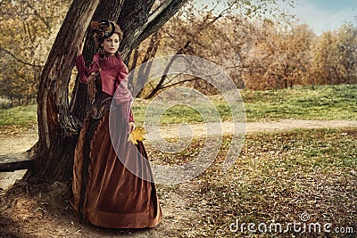 Woman in historical dress near the tree in autumn forest. Stock Photo