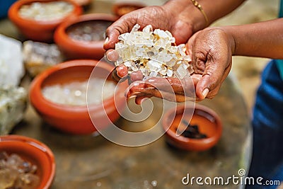 Woman hold washed mined gemstone, on table are many bowl with gemstone Stock Photo