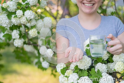Woman holding an antihistamine tablet and a glass of water while in a blooming garden. Stock Photo