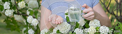 Woman holding an antihistamine tablet and a glass of water while in a blooming garden. Stock Photo