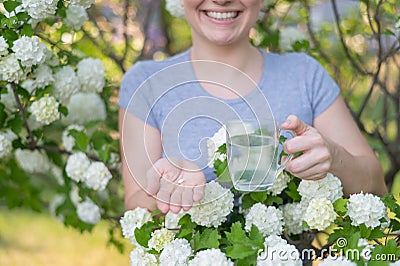 Woman holding an antihistamine tablet and a glass of water while in a blooming garden. Stock Photo