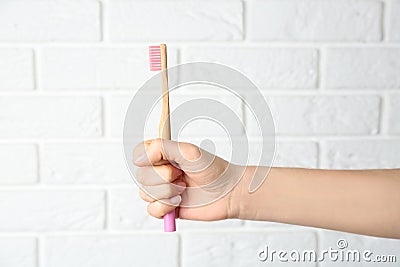 Woman holding bamboo toothbrush against brick wall, closeup Stock Photo