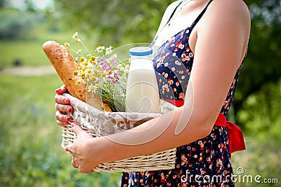 Woman holding a basket with bread, milk and flowers in a summer Stock Photo