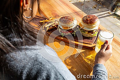 woman holding a beer, burgers and fries next to it Stock Photo