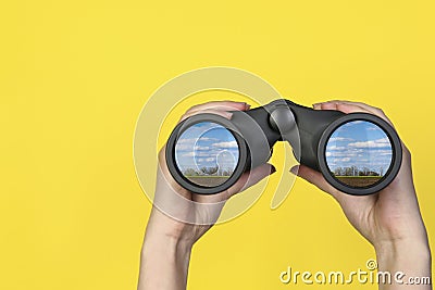 Woman holding binoculars on yellow background, closeup. Country landscape reflecting in lenses Stock Photo