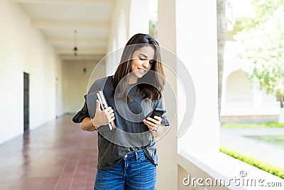 Woman Holding Books While Checking Social Site On Smartphone Stock Photo