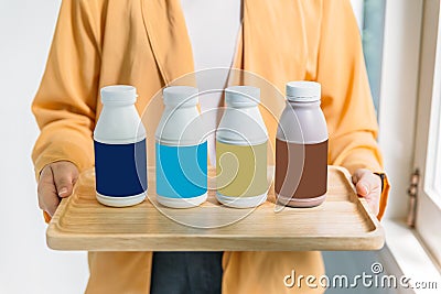 Woman holding bottles of pasteurized milk in blue, turquoise, gold and brown label color in wooden tray Stock Photo