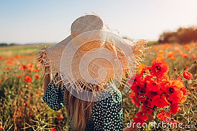 Woman holding bouquet of poppies flowers walking in summer field. Stylish girl in straw hat enjoys landscape Stock Photo