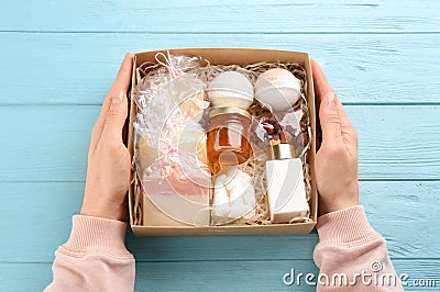 Woman holding box with stylish craft gift set at light blue wooden table, top view Stock Photo