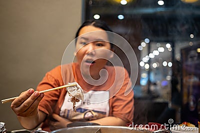 Woman holding chopsticks with a piece of meat in restaurant Stock Photo