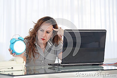 Woman holding a clock. Red-haired woman holds an alarm clock in her hand in the workplace Stock Photo