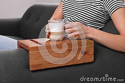 Woman holding cup of coffee on sofa armrest wooden table at home, closeup Stock Photo