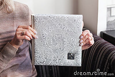 Woman holding a family photobook. White photo album in female hands. Wedding or family photoalbum with cover of genuine leather. Stock Photo