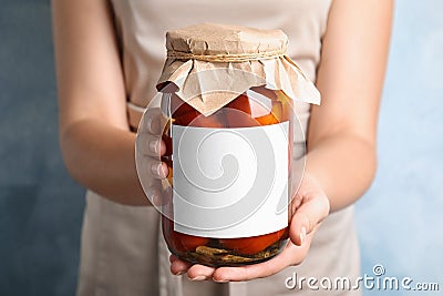 Woman holding glass jar of pickled tomatoes with blank sticker on blue background Stock Photo