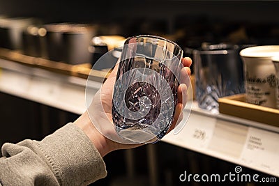 Woman holding glass from a shelf in homeware store. Stock Photo