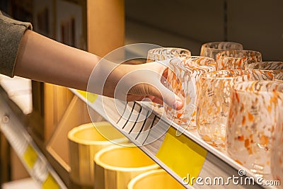 Woman holding glass from a shelf in homeware store. Stock Photo