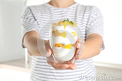 Woman holding glass of tasty peach dessert with yogurt in kitchen, closeup Stock Photo