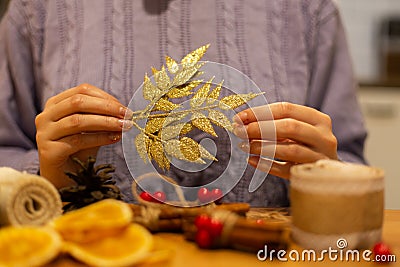 Woman holding gold festive, christmas, leaf ornament, diy decorations, blurry foreground, purple cable knit sweater in the Stock Photo