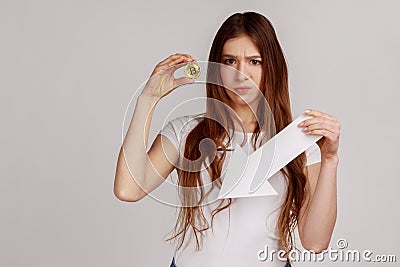 Woman holding golden bitcoin and white paper arrow, points down, showing downgrade of cryptocurrency Stock Photo
