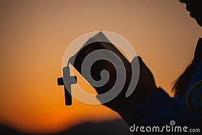 Woman holding a holy bible and cross in her hands and praying in the morning. Hands folded in prayer on a Holy Bible in church Stock Photo