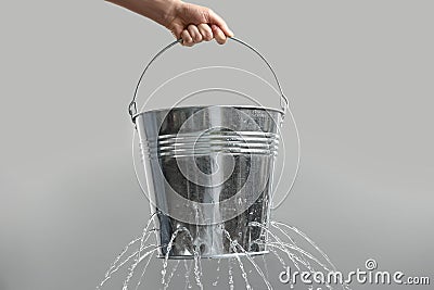 Woman holding leaky bucket with water on light grey background, closeup Stock Photo