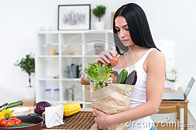 Woman holding paper bag with fresh grocery looking down attentively, choosing ingredients for diet healthy meal. Stock Photo