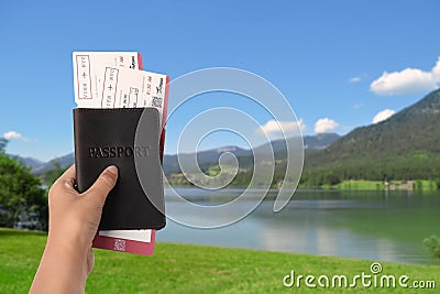 Woman holding passport with tickets near lake and mountains, closeup. Travel agency service Stock Photo