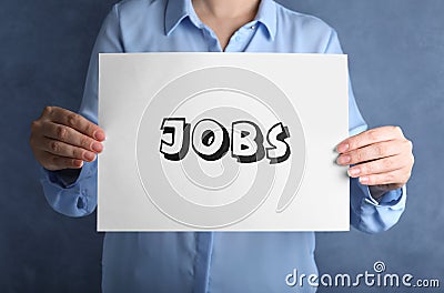 Woman holding sheet of paper with word JOBS on blue background. Career concept Stock Photo