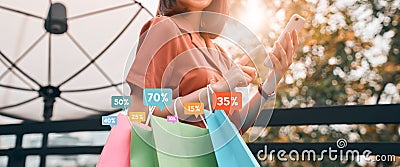 Woman holding shopping bags with show icon discount special offer promo and looking smartphone on the application online shop. Stock Photo