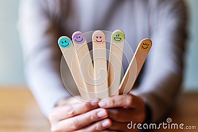 A female holding and showing colorful hand draw happy emotion faces on wooden stick Stock Photo