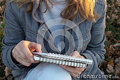 Woman in holding sketchbook and a pencil outdoors. Close-up of hands with notebook and pencil. Drawing, writing, learning Stock Photo
