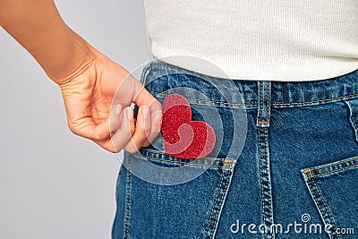 Woman holding a small sparkling red heart putting it in or taking off the pocket of her jeans. Sharing and receiving Stock Photo