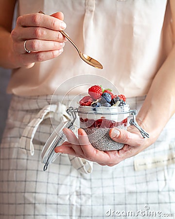A woman holding a spoon and a mason jar with chai pudding topped with fresh berry fruit Stock Photo