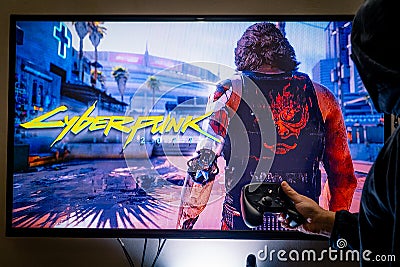 Woman holding a steam controller and playing popular video game Cyberpunk 2077 on a television and PC Editorial Stock Photo