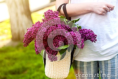 Woman holding straw bag with vivid bunch of lilac flowers Stock Photo