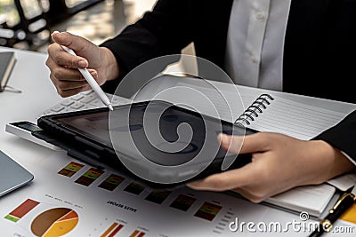 Woman holding a tablet at a screen showing company financial status chart, a finance worker is reviewing a document to send a Stock Photo