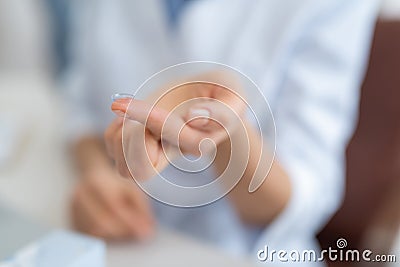 Woman holding transparent contact lens on blurred background Stock Photo