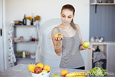 Woman holds in hand cake sweet bun and apple fruit choosing, trying to resist temptation, make the right dietary choice. Weight lo Stock Photo