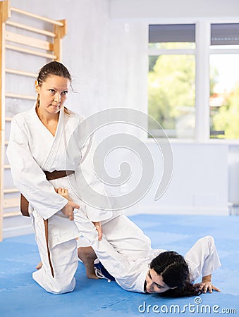 Sportive woman holds her opponent by force while sitting on mats during judo classes Stock Photo