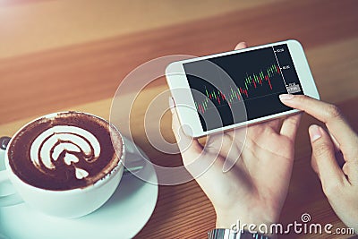 The woman holds the phone on a table with a graphical screen to invest the stock`s value. Investment concepts that rely on decisi Stock Photo