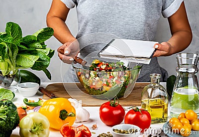 Woman holds recipe book with place for text in her hand and cooking healthy food in the kitchen. Healthy vegan food Stock Photo