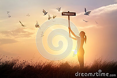 Woman holds a sign with word freedom and flying birds on sunset Stock Photo