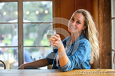 Woman holds up a pint of light beer or cider wine and cheers, in a beautiful sunny pub brewery Stock Photo