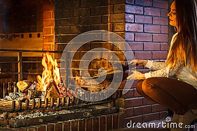 Woman at home fireplace making fire with bellows. Stock Photo